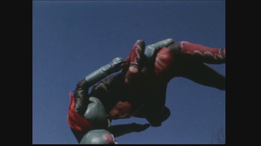 快晴の青空の下、空中で激しくもつれ合いながら格闘する仮面ライダー1号と蝙蝠男のスタントシーン